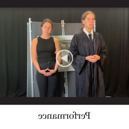 Labeled ‘Performance.’ A still from a video showing two students standing side by side. One is wearing a tie and a black robe, and the other is wearing all black.